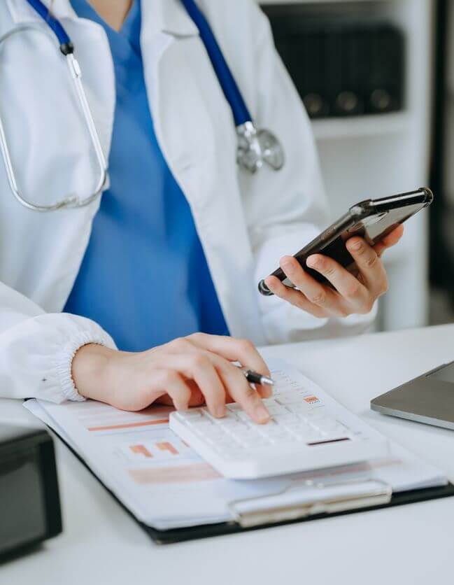 Ärztin sitzt am Schreibtisch rechnet und kalkuliert